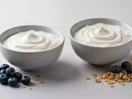 Zwei minimalistische Schalen mit Naturjoghurt und griechischem Joghurt, garniert mit Blaubeeren und Müsli, auf hellem Hintergrund. - Foto: über boerse-global.de