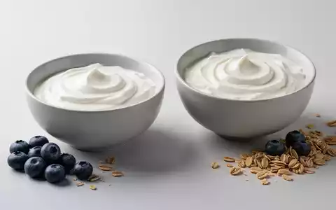 Zwei minimalistische Schalen mit Naturjoghurt und griechischem Joghurt, garniert mit Blaubeeren und Müsli, auf hellem Hintergrund. - Foto: über boerse-global.de