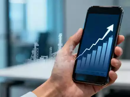 Eine Hand hält ein Smartphone mit einem Aktienchart und einer Fabriksilhouette im Hintergrund in einem modernen Büro. - Foto: über boerse-global.de