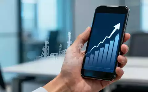 Eine Hand hält ein Smartphone mit einem Aktienchart und einer Fabriksilhouette im Hintergrund in einem modernen Büro. - Foto: über boerse-global.de