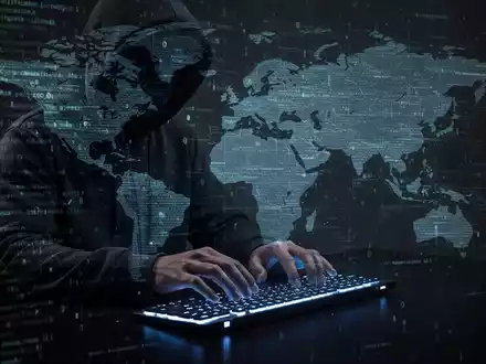 A shadowy figure in a hoodie typing on a keyboard, with digital code and a world map overlay, symbolizing cybercrime. - Foto: über boerse-global.de