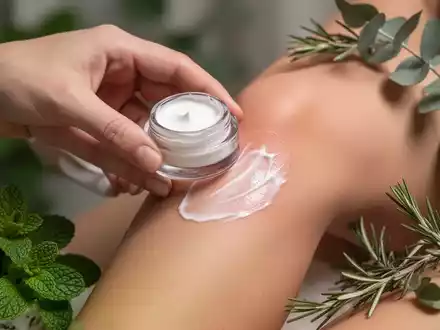 Eine Hand trägt eine pflanzliche Schmerzcreme auf ein Gelenk auf, mit unscharfen botanischen Elementen im Hintergrund. - Foto: über boerse-global.de
