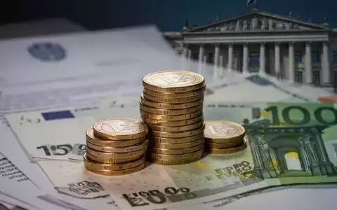 Ein Nahaufnahme-Bild von gestapelten Euro-Münzen und Banknoten, mit unscharfem Hintergrund von Dokumenten und einem Regierungsgebäude. - Foto: über boerse-global.de