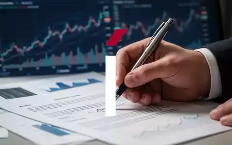 Eine Hand unterschreibt ein Dokument mit einem Stift, mit unscharfen Finanzdiagrammen im Hintergrund. - Foto: über boerse-global.de