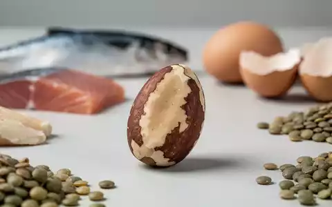 Eine einzelne Paranuss im Vordergrund, unscharf im Hintergrund sind Fisch, Eier und Linsen zu sehen. Fokus auf gesunde Ernährung. - Foto: über boerse-global.de