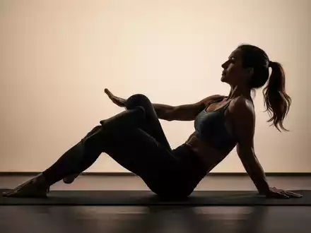 Eine Frau in Sportkleidung führt eine Pilates-Übung auf einer Matte aus, die die Rumpfmuskulatur stärkt. - Foto: über boerse-global.de