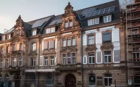 Historische deutsche Wohnhausfassade mit sichtbaren Sanierungsarbeiten und modernen Energieeffizienz-Elementen. - Foto: über boerse-global.de