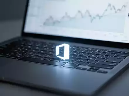 Close-up of a laptop keyboard with a subtle Microsoft Office logo on a key, screen blurred with a financial chart. - Foto: über boerse-global.de