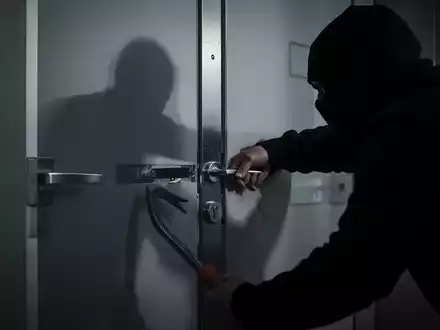 Eine dunkle Gestalt versucht, eine moderne Wohnungstür mit einer Brechstange aufzubrechen. Der Fokus liegt auf dem Schlossbereich. - Foto: über boerse-global.de