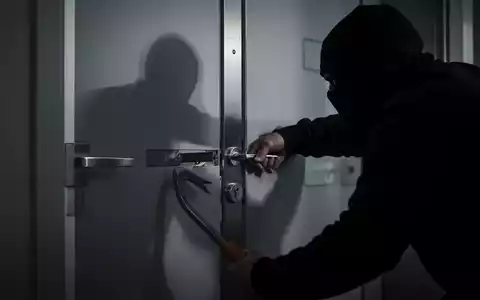 Eine dunkle Gestalt versucht, eine moderne Wohnungstür mit einer Brechstange aufzubrechen. Der Fokus liegt auf dem Schlossbereich. - Foto: über boerse-global.de