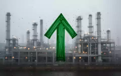 Ein grüner Pfeil zeigt auf einer beschlagenen Fensterscheibe nach oben, mit einer verschwommenen Industrieanlage im Hintergrund. - Foto: über boerse-global.de