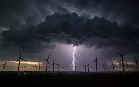 Dunkle Sturmwolken über einem Windpark bei Sonnenuntergang, mit einem einzelnen Blitz in der Ferne, der Spannung und finanzielle Volatilität symbolisiert. - Foto: über boerse-global.de