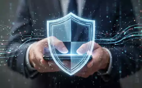 A glowing digital shield icon overlaid on a blurred image of hands using a smartphone, with data streams. - Foto: über boerse-global.de