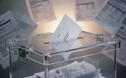 Eine transparente Wahlurne mit einem einzelnen Stimmzettel vor einem verschwommenen Hintergrund von Finanzdokumenten. - Foto: über boerse-global.de