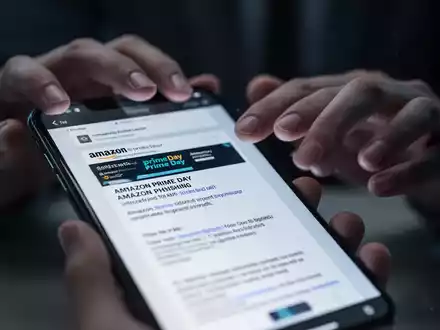 Nahaufnahme eines Smartphone-Bildschirms, der eine gefälschte Amazon Prime Day Phishing-E-Mail anzeigt, mit unscharfen Händen im Hintergrund. - Foto: über boerse-global.de
