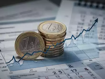 Ein Stapel deutscher Euro-Münzen vor einem Finanzdiagramm, das einen Aufwärtstrend zeigt, mit verschwommenen Dokumenten und einem Kalender im Hintergrund. - Foto: über boerse-global.de