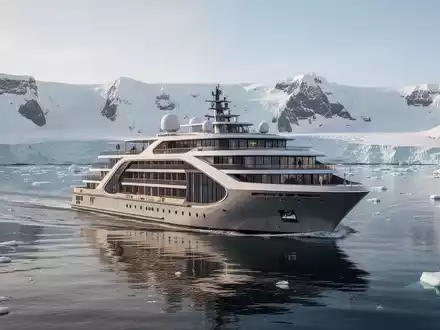 Ein modernes Expeditions-Kreuzfahrtschiff gleitet durch ruhiges, blaues Wasser vor einer eisigen, unberührten Küstenlandschaft unter klarem Himmel. - Foto: über boerse-global.de