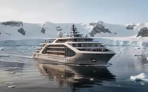 Ein modernes Expeditions-Kreuzfahrtschiff gleitet durch ruhiges, blaues Wasser vor einer eisigen, unberührten Küstenlandschaft unter klarem Himmel. - Foto: über boerse-global.de