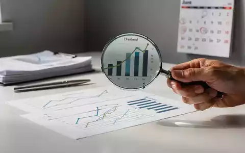 Eine Hand hält eine Lupe über einen Finanzbericht mit Dividendendiagrammen, im Hintergrund ein Kalender, der den Juni hervorhebt. - Foto: über boerse-global.de