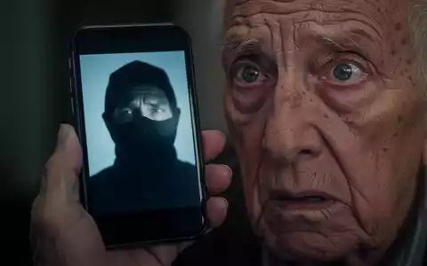Eine ältere Person hält ein Smartphone, auf dessen Bildschirm das unscharfe Gesicht eines Betrügers zu sehen ist, das sich im besorgten Auge spiegelt. - Foto: über boerse-global.de