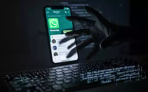 Eine Nahaufnahme eines Smartphones mit WhatsApp, eine dunkle Hand greift aus dem Bildschirm nach einer Computertastatur. - Foto: über boerse-global.de