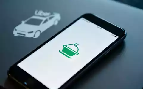 Smartphone mit einer Essensliefer-App, im Hintergrund verschwommen ein Uber-Auto-Symbol, das eine Beteiligung andeutet. - Foto: über boerse-global.de