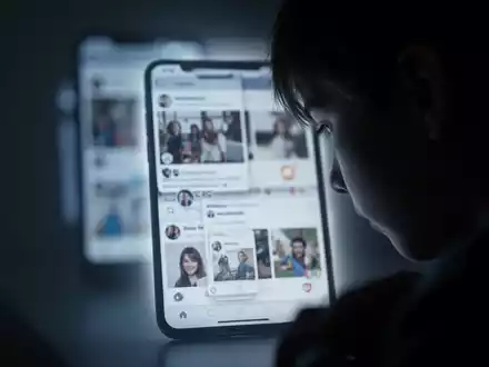 Eine Silhouette eines jungen Menschen, der auf einen leuchtenden Smartphone-Bildschirm blickt, der soziale Medien anzeigt. - Foto: über boerse-global.de