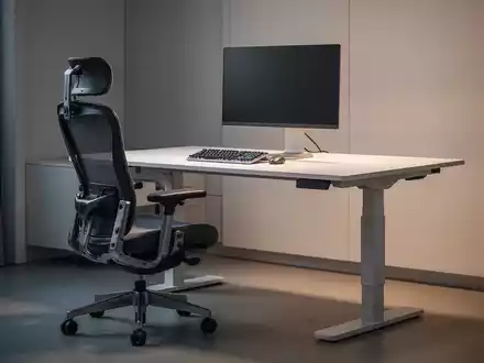 Ein modernes Home-Office mit einem höhenverstellbaren Schreibtisch und einem ergonomischen Bürostuhl, beleuchtet durch sanftes Licht. - Foto: über boerse-global.de