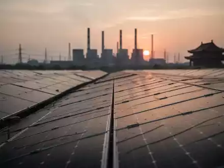 Solarpanel-Felder bei Sonnenuntergang mit einer verschwommenen Silhouette eines Kraftwerks am Horizont. - Foto: über boerse-global.de