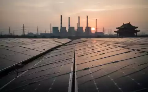 Solarpanel-Felder bei Sonnenuntergang mit einer verschwommenen Silhouette eines Kraftwerks am Horizont. - Foto: über boerse-global.de