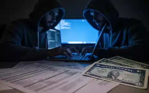 A shadowy figure typing on a laptop, with blurred financial documents and a Social Security card in the foreground. - Foto: über boerse-global.de