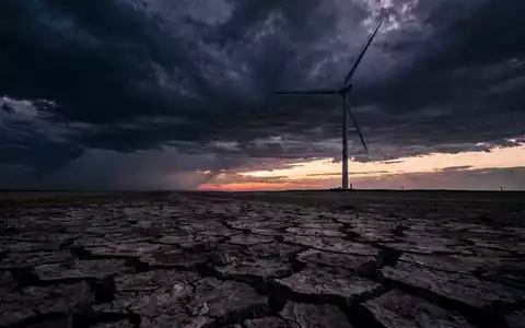 Eine einzelne Windturbine vor einem stürmischen Himmel, der Boden ist rissig und trocken. Symbolisiert Druck nach starkem Lauf. - Foto: über boerse-global.de