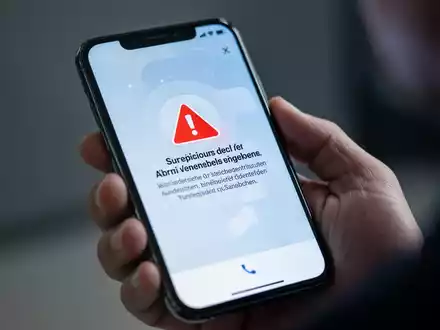 Ein Smartphone-Bildschirm zeigt eine Warnmeldung auf Deutsch über einen verdächtigen Anruf, im Hintergrund eine unscharfe Hand, die das Telefon hält. - Foto: über boerse-global.de