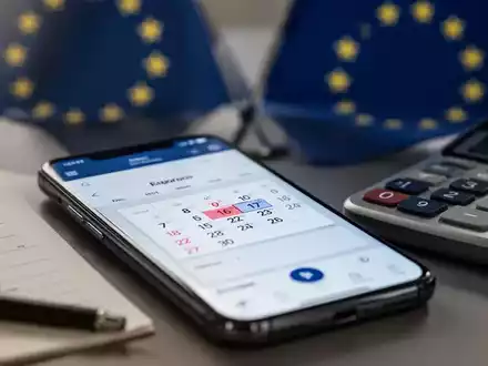 Nahaufnahme eines Smartphones mit Kalender-App, Taschenrechner und angedeuteter EU-Flagge, symbolisiert rechtliche und finanzielle Änderungen. - Foto: über boerse-global.de