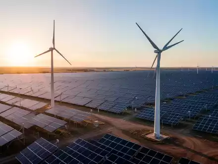 Eine riesige Solaranlage mit einer Windkraftanlage im Vordergrund bei Sonnenuntergang, symbolisiert erneuerbare Energien und Investitionen. - Foto: über boerse-global.de