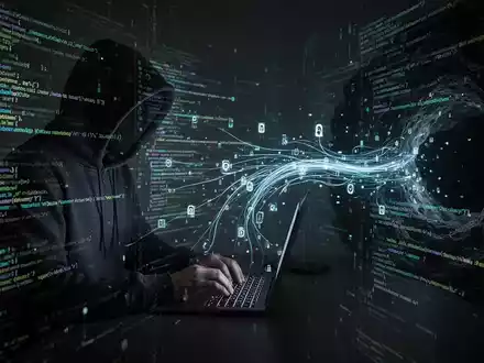 A shadowy figure in a hoodie typing on a laptop, surrounded by glowing lines of code and digital data streams, symbolizing a cyberattack. - Foto: über boerse-global.de