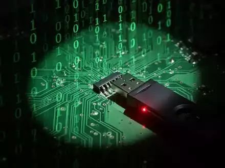 A glowing green circuit board with binary code, an ominous shadow, and a USB drive emitting a red light. - Foto: über boerse-global.de