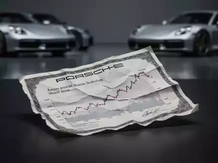 Eine zerknitterte Porsche-Aktie auf einer dunklen Oberfläche, im Hintergrund verschwommene Porsche-Fahrzeuge. - Foto: über boerse-global.de