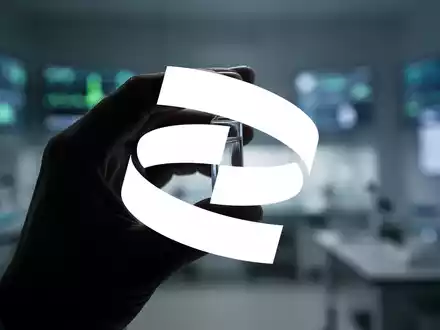 Eine einzelne Hand hält ein klares Glasfläschchen, teilweise im Schatten, vor einem verschwommenen Laborhintergrund. - Foto: über boerse-global.de