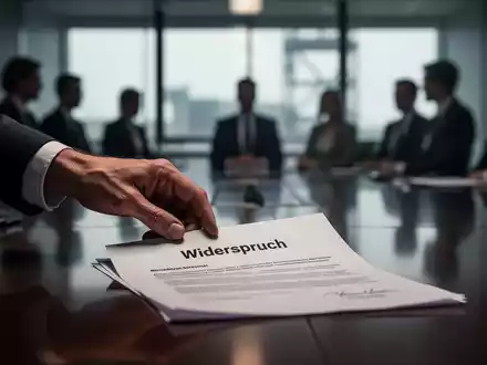 Eine Hand legt ein Dokument mit der Aufschrift „Widerspruch“ auf einen Konferenztisch, im Hintergrund verschwommene Silhouetten von Personen. - Foto: über boerse-global.de