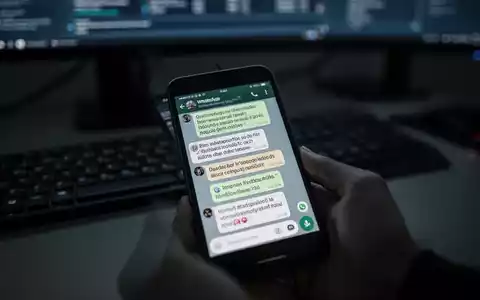 A close-up of a smartphone screen displaying suspicious WhatsApp messages in a dimly lit office setting, symbolizing digital fraud and cybercrime. - Foto: über boerse-global.de