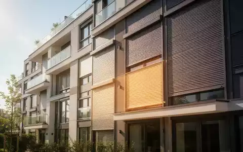 Eine moderne Wohnhausfassade mit teilweise heruntergelassenen Rollläden an den Fenstern, die Licht durchlassen. - Foto: über boerse-global.de