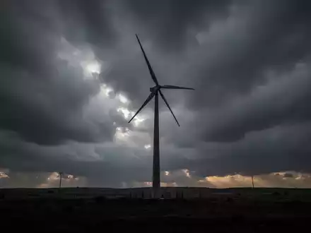 Eine einzelne Windkraftanlage vor einem stürmischen Himmel, die langfristige Energieprojekte symbolisiert. - Foto: über boerse-global.de