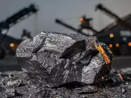 Nahaufnahme eines großen, rohen Graphiterzbrockens mit unscharfem Hintergrund von Bergbauausrüstung. - Foto: über boerse-global.de