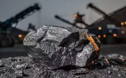 Nahaufnahme eines großen, rohen Graphiterzbrockens mit unscharfem Hintergrund von Bergbauausrüstung. - Foto: über boerse-global.de