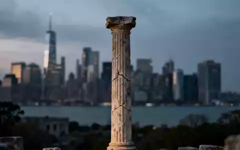 Eine antike griechische Säule vor dem unscharfen Hintergrund einer modernen Finanzskyline bei Dämmerung. - Foto: über boerse-global.de
