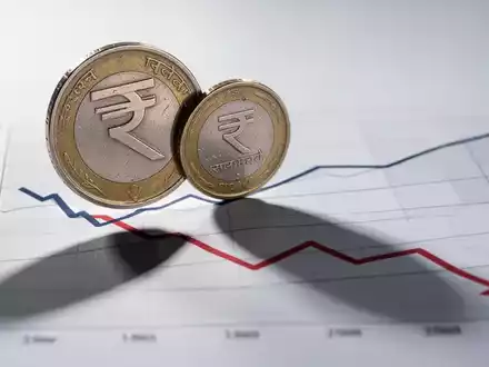 Eine indische Rupienmünze wirft einen langen Schatten auf ein Diagramm mit einem Abwärtstrend, das Dividenden trotz Verlusten symbolisiert. - Foto: über boerse-global.de