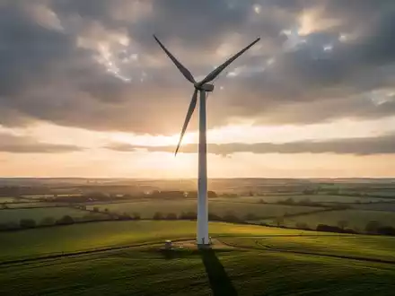 Eine große, moderne Windkraftanlage mit sich drehenden Rotorblättern vor einem dramatischen Himmel bei Sonnenuntergang. - Foto: über boerse-global.de