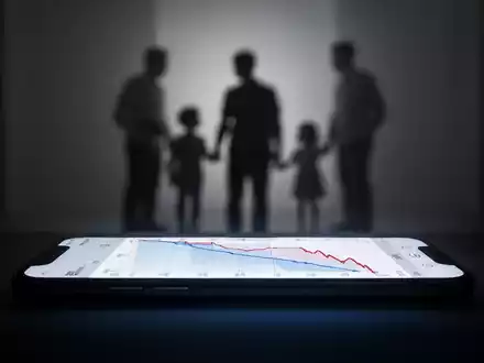 A glowing smartphone screen displaying a declining graph, subtly contrasted with a blurred family silhouette in the background. - Foto: über boerse-global.de