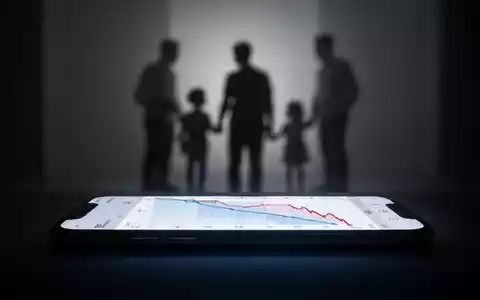 A glowing smartphone screen displaying a declining graph, subtly contrasted with a blurred family silhouette in the background. - Foto: über boerse-global.de